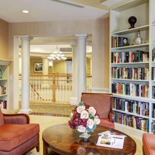 A cozy reading area with bookshelves filled with books, comfortable chairs, and a table with a flower arrangement.