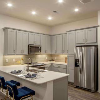 A modern kitchen with gray cabinets, stainless steel appliances, and a central island with blue bar stools under recessed lighting.
