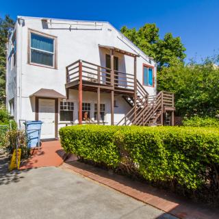 A two-story house with a spacious backyard, featuring a wooden staircase and surrounded by greenery.