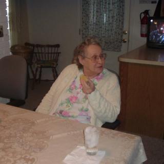 An elderly person seated at a table in a living room setting.