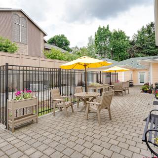 An outdoor patio area with tables, chairs, and yellow umbrellas set on a brick floor.