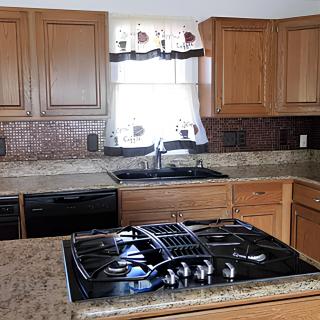 A modern kitchen with a stove, wooden cabinets, and a window above the sink.