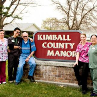 A group of people posing together in front of a sign for Kimball County Manor.