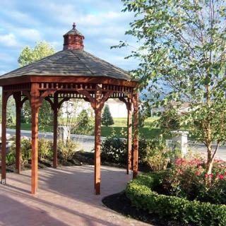 A wooden gazebo surrounded by a landscaped garden and trees.