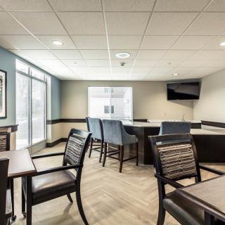 A modern conference room with tables, chairs, and a TV screen under ample natural light.