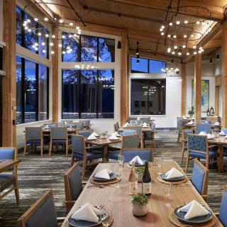 Elegant dining area in a restaurant with well-arranged tables and large windows overlooking an evening view.