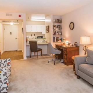 A cozy living space featuring a small desk, comfortable sofa, and a kitchenette in the background.