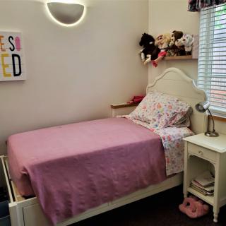 A cozy child's bedroom with a single bed, purple bedspread, stuffed animals, and a nightstand with a lamp.