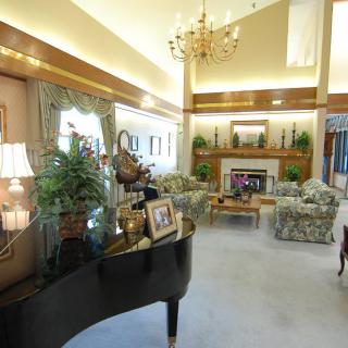A spacious living room featuring a grand piano, elaborate chandelier, and cozy fireplace.