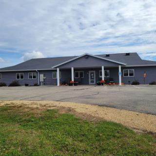 A single-story residential building with a driveway and lawn under a cloudy sky.