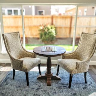 A cozy seating arrangement featuring two elegant chairs and a round table, inviting a moment of relaxation with natural light streaming in through the window.