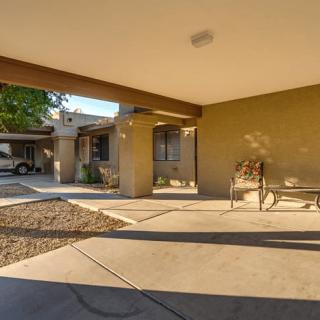 A modern house featuring a spacious covered patio with outdoor seating and warm sunlight casting shadows.