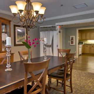 A warmly lit dining room featuring a wooden table and chairs, with a chandelier overhead.