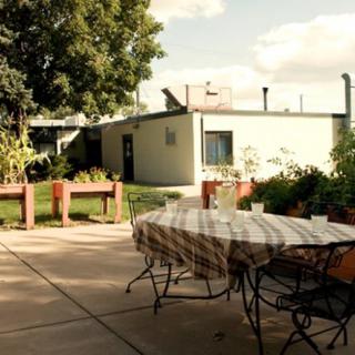 A cozy outdoor patio area with a table and chairs, surrounded by greenery and trees.