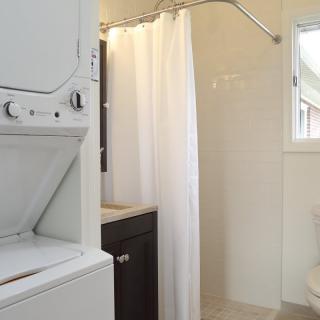 A small bathroom with a shower and stacked washer and dryer.