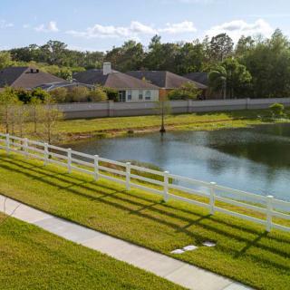 A scenic view of a small lake surrounded by a white fence, with houses and trees in the background.