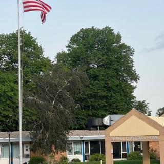 A view of a building with an American flag waving in front, surrounded by trees under a clear blue sky.