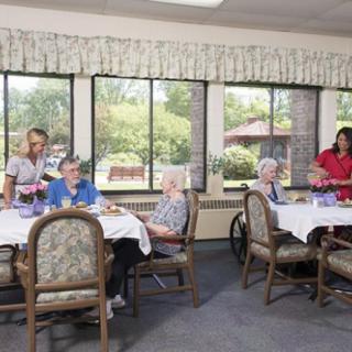 Elderly residents enjoy a meal in a nursing home dining room with staff assistance.