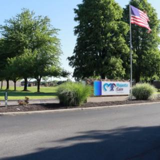 A scenic outdoor view featuring a company sign, an American flag, and lush green trees lining a road.