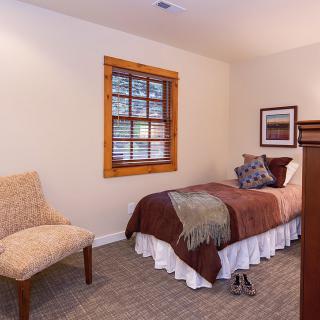 A cozy bedroom with a single bed, a chair, and a window featuring wooden blinds.