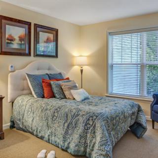 A cozy bedroom with a well-decorated bed, artwork on the wall, and natural light coming through the window.