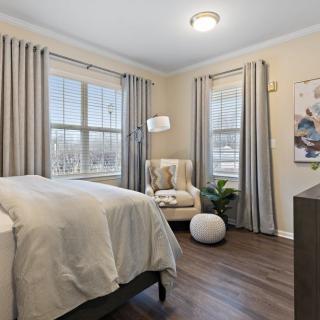 A bright and cozy bedroom with modern decor, featuring a large bed, armchair, and elegant curtains.