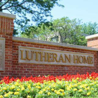 A sign for Lutheran Home on a brick wall surrounded by colorful flowers.