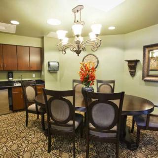 A cozy dining area with a round table, elegant chairs, and a chandelier, complemented by a kitchenette and a decorative flower arrangement.