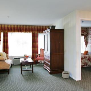 A cozy living room area with a sofa, table, and cabinet, featuring large windows with curtains.