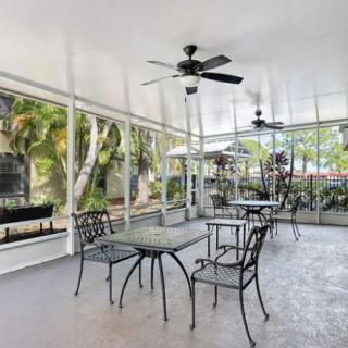 An enclosed outdoor patio with tables, chairs, and ceiling fans, overlooking a lush garden.