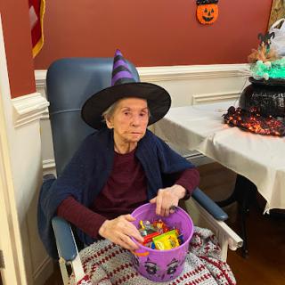 An elderly person dressed in a witch costume, ready to celebrate Halloween with a bucket of candy.