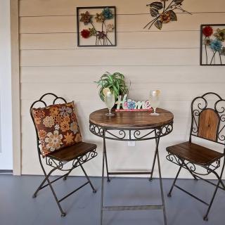 A cozy outdoor patio setup with a round table, two ornate chairs, wall decorations, and a potted plant.