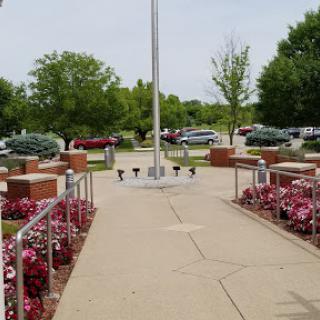 A serene park setting featuring a flagpole surrounded by vibrant flowers and lush greenery.