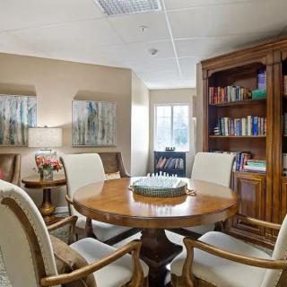 A cozy meeting room with a wooden round table surrounded by chairs and a bookshelf filled with books.