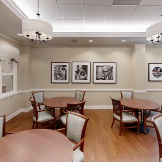 A well-lit dining area featuring round tables and cushioned chairs, adorned with framed artwork on a neutral-toned wall.