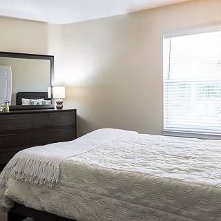 A neatly made bed in a well-lit bedroom with a dresser and mirror.