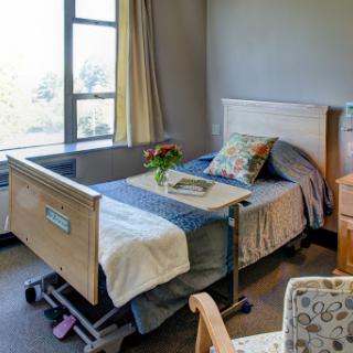 A serene hospital room featuring a neatly made bed, a window with natural light, and a small vase of flowers.