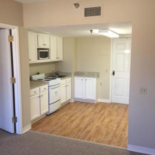 A cozy kitchen area in a modern apartment featuring white cabinetry and wooden flooring.