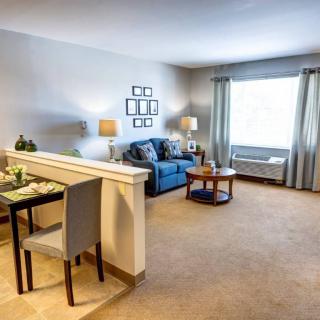 A cozy living room with a small dining area, featuring a comfortable sofa, lamps, and large windows.