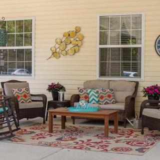 A cozy patio setup with outdoor furniture including a sofa, chairs, a coffee table, and decorative elements like plants and wall art.