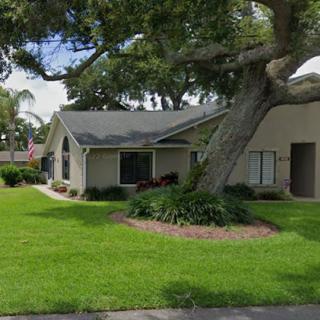 A suburban house with a well-maintained lawn and a large tree in the yard.