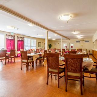 A spacious dining area with wooden tables and chairs, featuring large windows with red curtains.