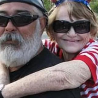An elderly couple enjoying a sunny day together, both wearing sunglasses and smiling.