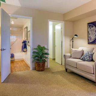 A cozy living room with a sofa, potted plant, and an open door leading to another room.