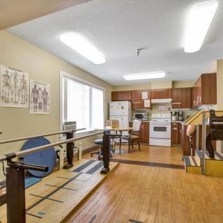 A room featuring a kitchen area combined with rehabilitation equipment, showcasing wooden floors and bright lighting.