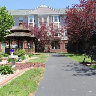 A charming building surrounded by a well-maintained garden with a pathway leading to a gazebo.