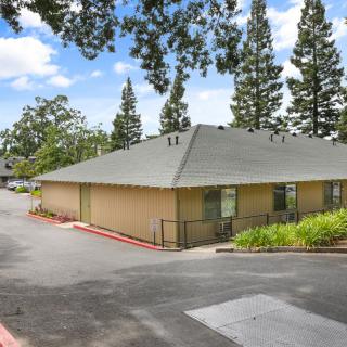A single-story building surrounded by trees and a road under a clear blue sky.