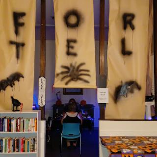 A spooky library adorned with Halloween decorations, including banners featuring a spider and eerie motifs.
