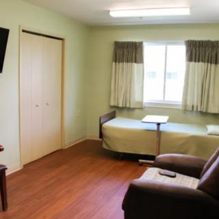 A simple room with a bed, chair, and television.