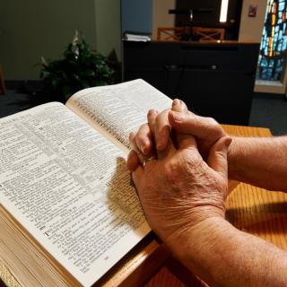 Hands clasped in prayer over an open Bible.